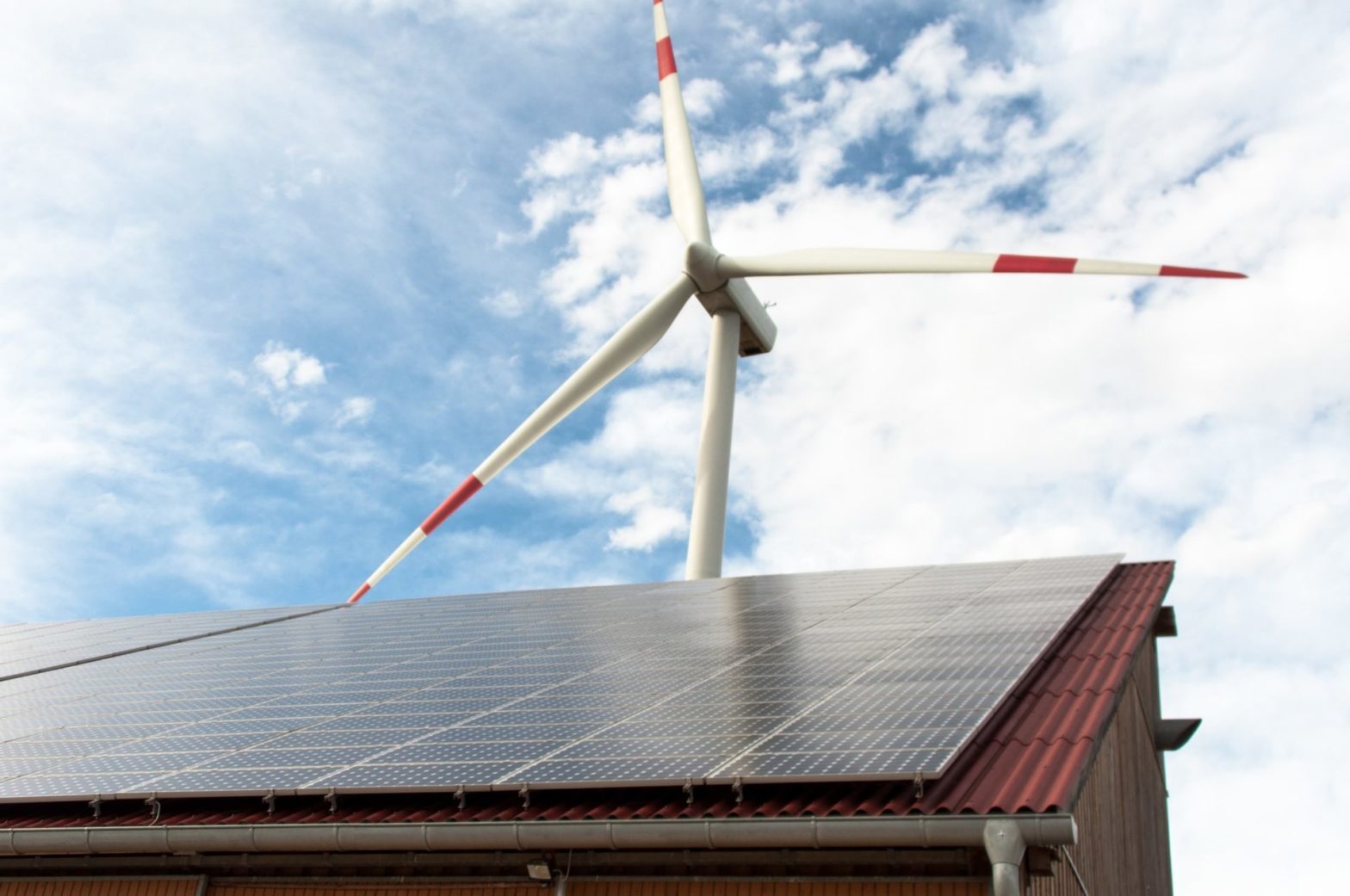 Alternative Energien: Solarzellen auf Scheunendach mit Windrad im Hintergrund